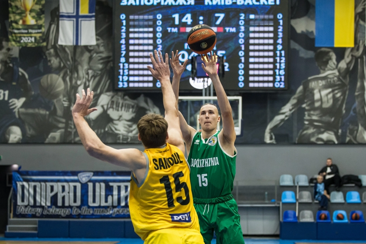 Basketball action in the Superliga: a player in green shoots as an opponent defends. Highlights competitive performances.