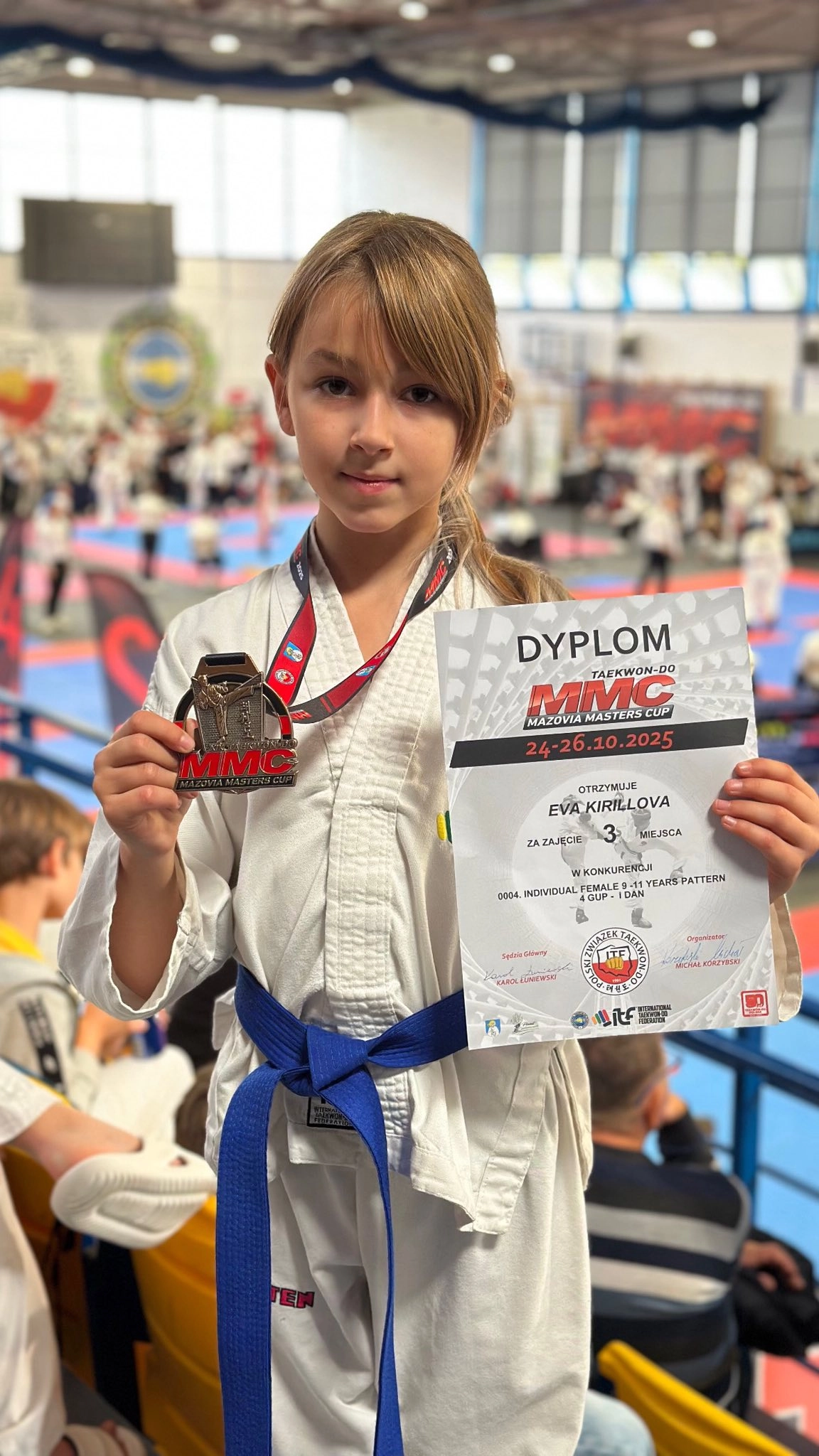 Дівчина в кімоно з медаллю та дипломом на турнірі з Таеквон-До «Mazovia Master Cup 2025» у Польщі.