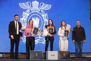 Група людей на сцені з нагородами на фоні синього екрану з емблемою, святковий захід