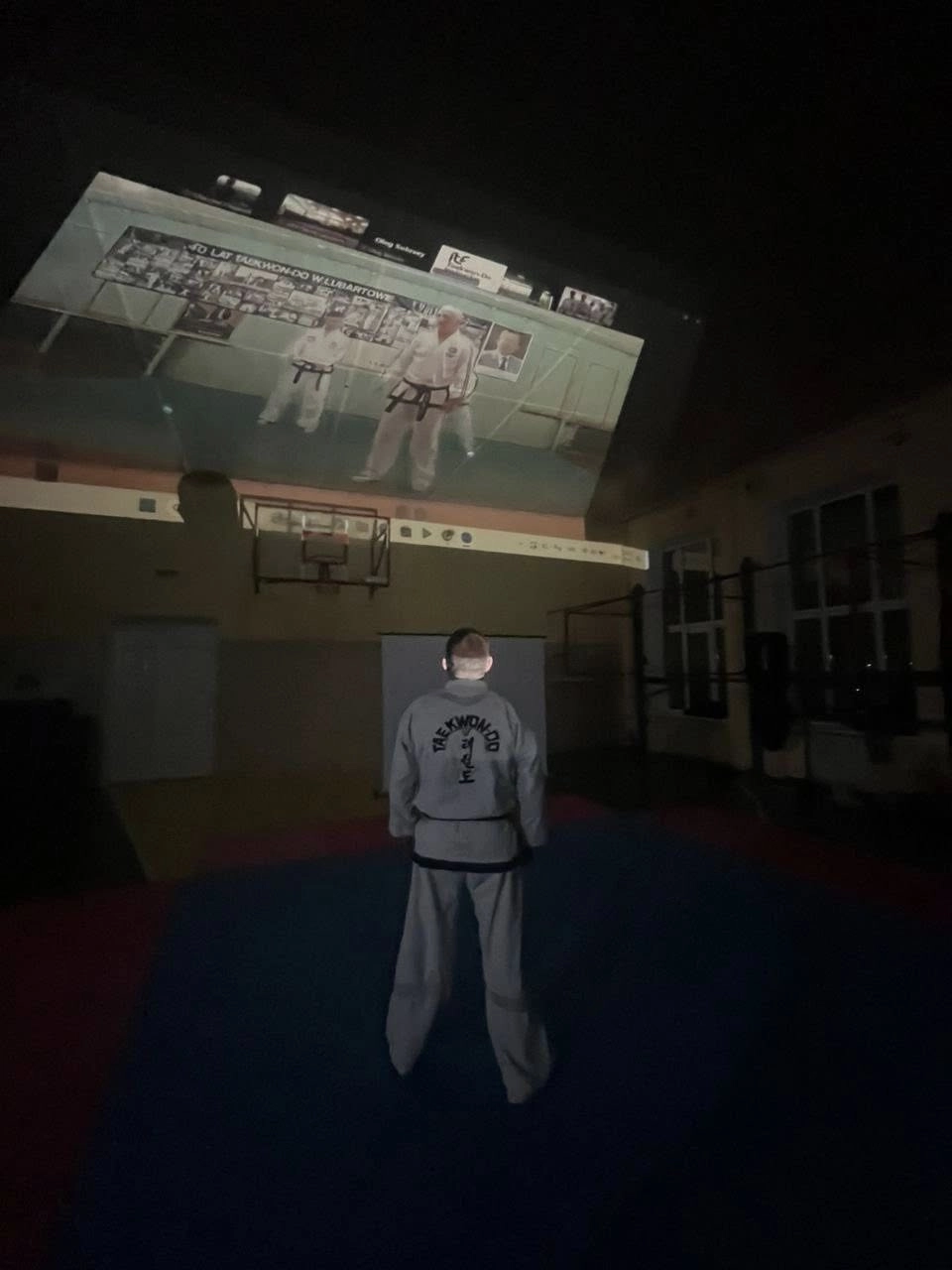 Інструктор у кімоно дивиться на проекцію онлайн-курсу з Таеквон-До на стіні спортивного залу