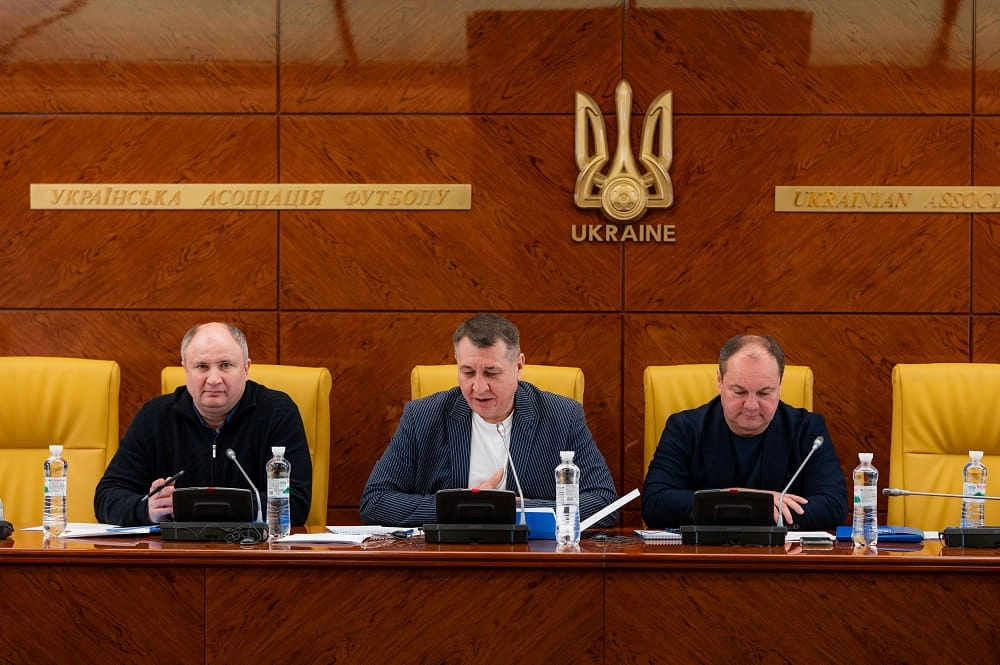 Три чоловіки за столом на засіданні Комітету масового футболу УАФ, на задньому плані логотип асоціації