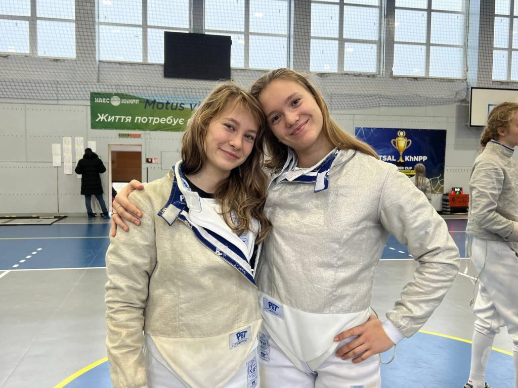 Дві юні фехтувальниці у спортивному залі після змагань, святкуючи участь у турнірі на шаблях у Нетішині.