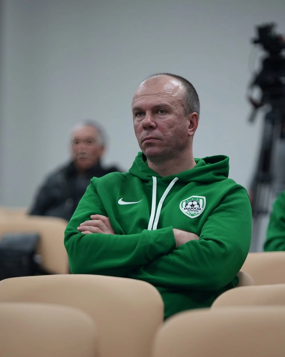 Чоловік у зеленій спортивній кофті сидить на форумі АФДО у Дніпрі, уважно слухаючи лекцію