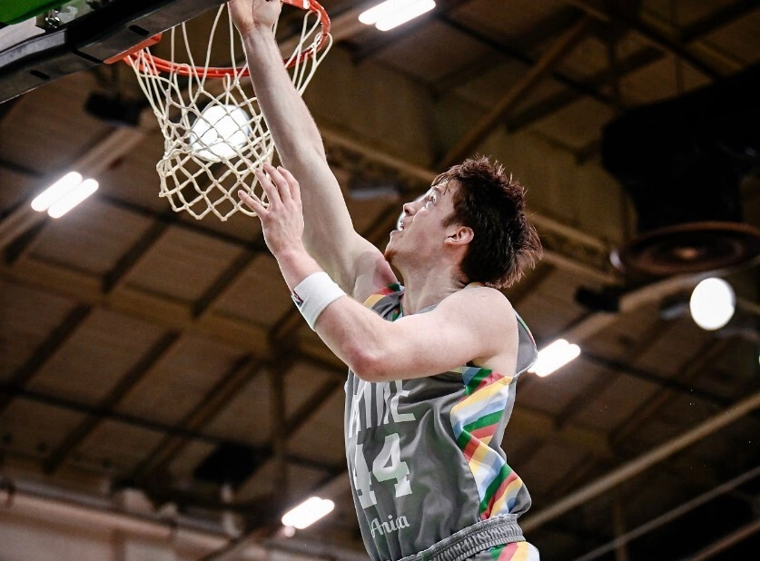 Basketball player scoring a dunk during a match, showcasing athleticism and competitive spirit in a sports arena.