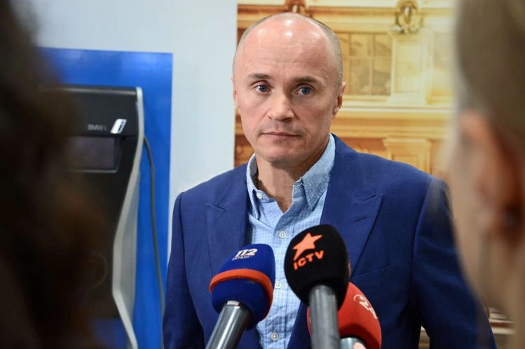Чоловік у синьому піджаку дає інтерв'ю на фоні мікрофонів з логотипами телеканалів