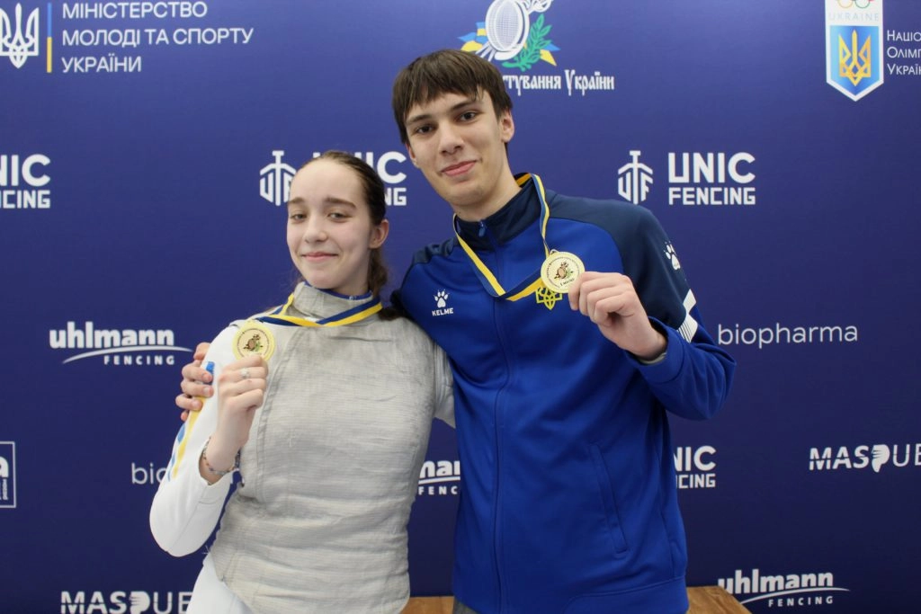 Юні чемпіони України з фехтування на рапірах тримають золоті медалі на фоні банера змагань