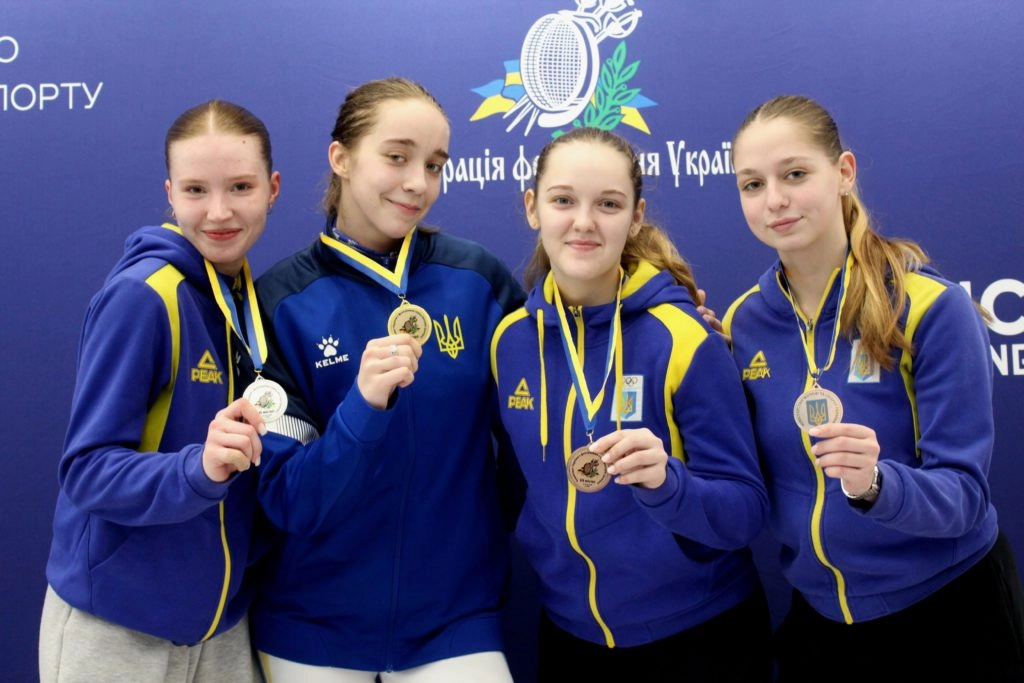 Чотири юніорки з медалями на чемпіонаті України з фехтування на рапірах, усміхнені на фоні банера
