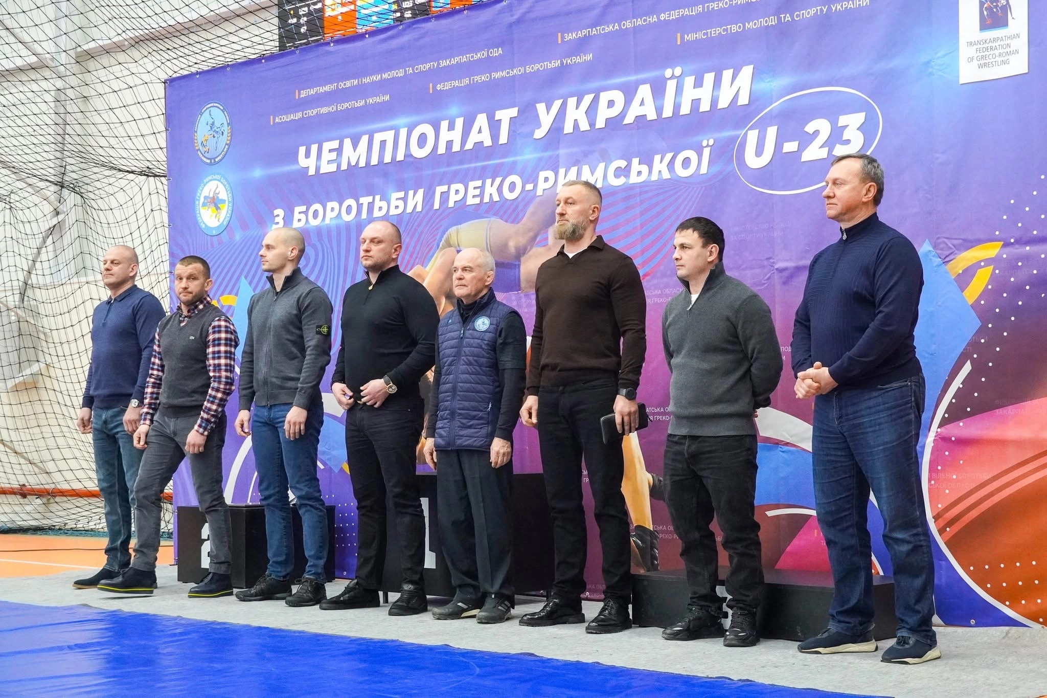 Чоловіки стоять на сцені перед банером чемпіонату України з греко-римської боротьби U23 в Ужгороді