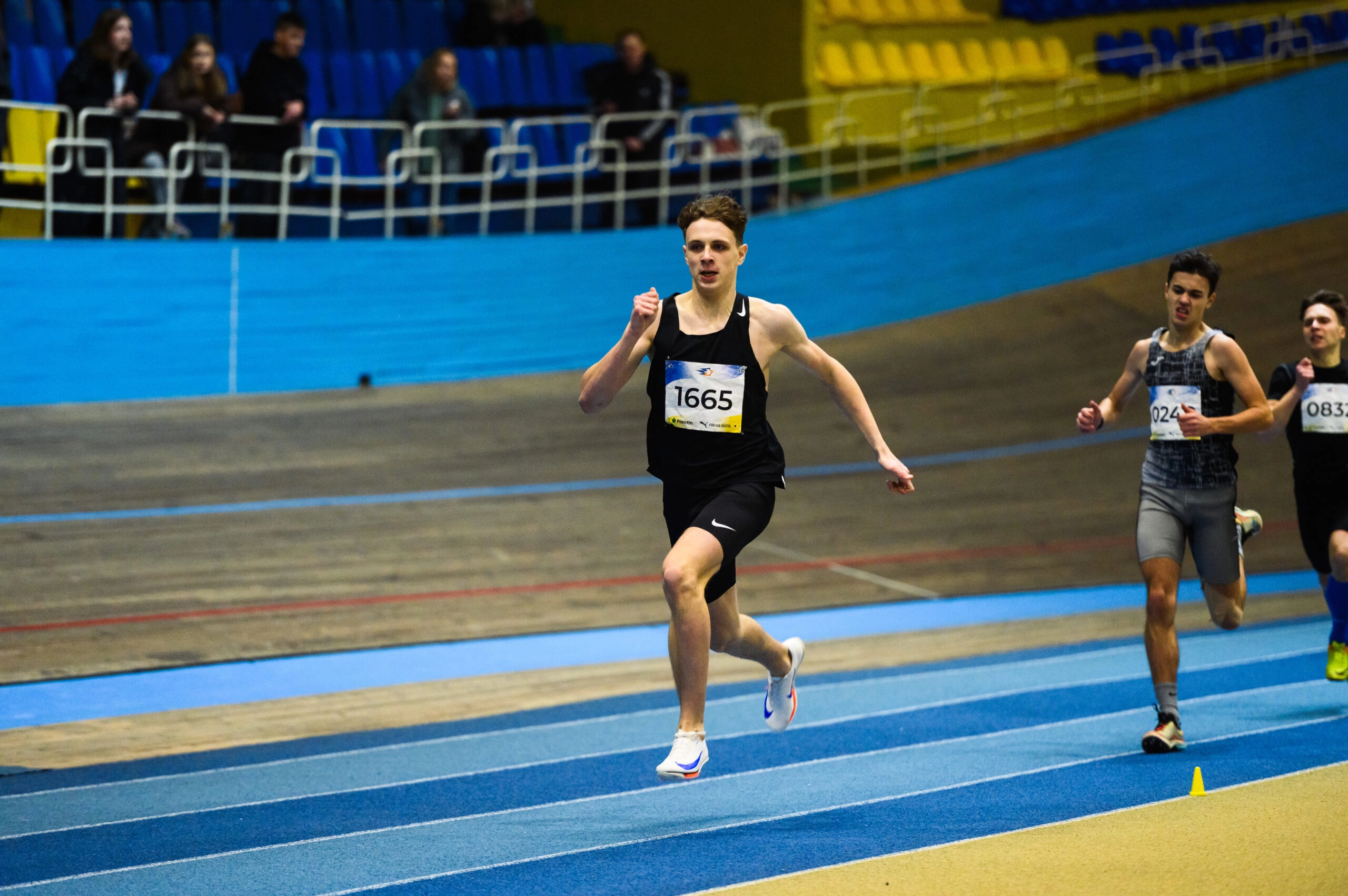Юний спортсмен біжить на змаганнях з легкої атлетики в приміщенні, тримаючи лідерство на дистанції