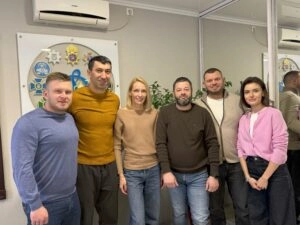 Група людей стоїть разом у приміщенні з дзеркалом, на стіні висить емблема спортивної організації