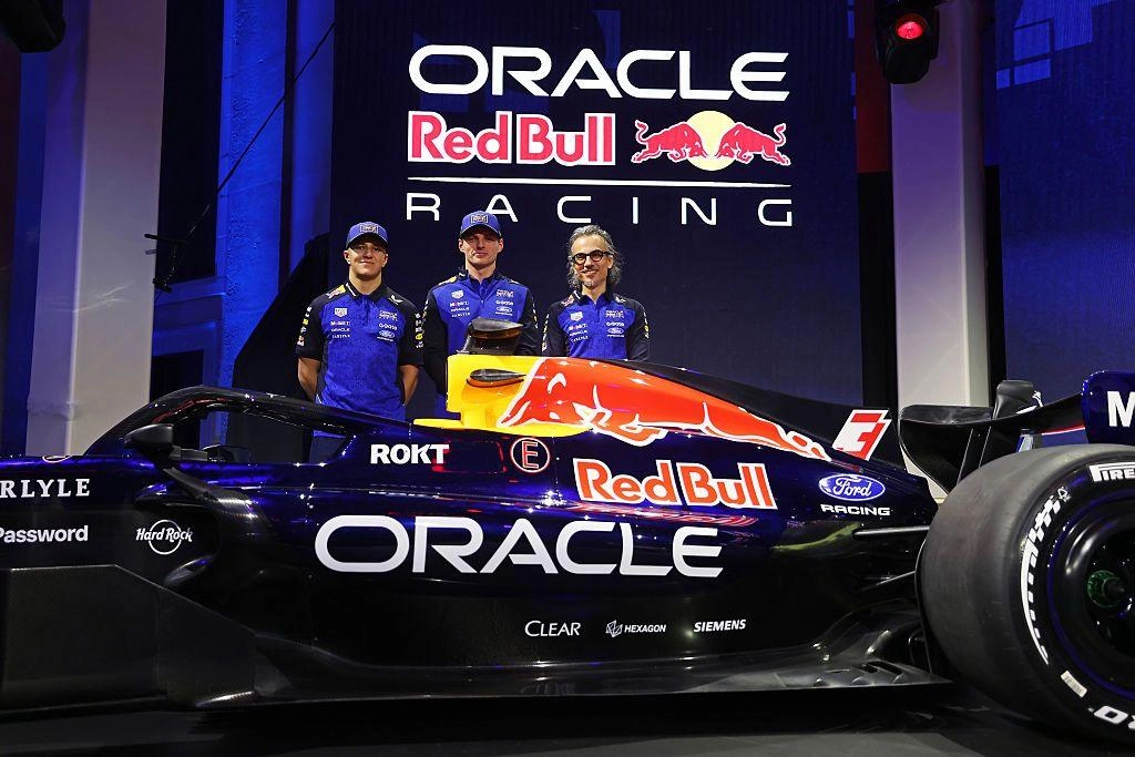 Гоночний болід Red Bull на презентації команди з трьома людьми в синьому одязі на фоні логотипів Oracle та Red Bull