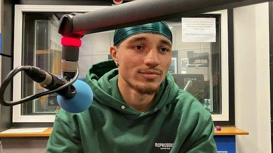 Молодий чоловік у зеленій худі сидить перед мікрофоном у радіостудії