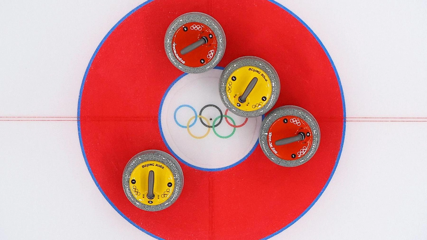 Чотири камені для керлінгу на льодовій доріжці з олімпійськими кільцями в центрі мішені