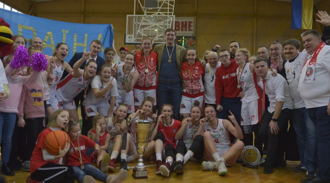 Жіноча баскетбольна команда святкує перемогу з кубком на спортивному майданчику, оточена вболівальниками