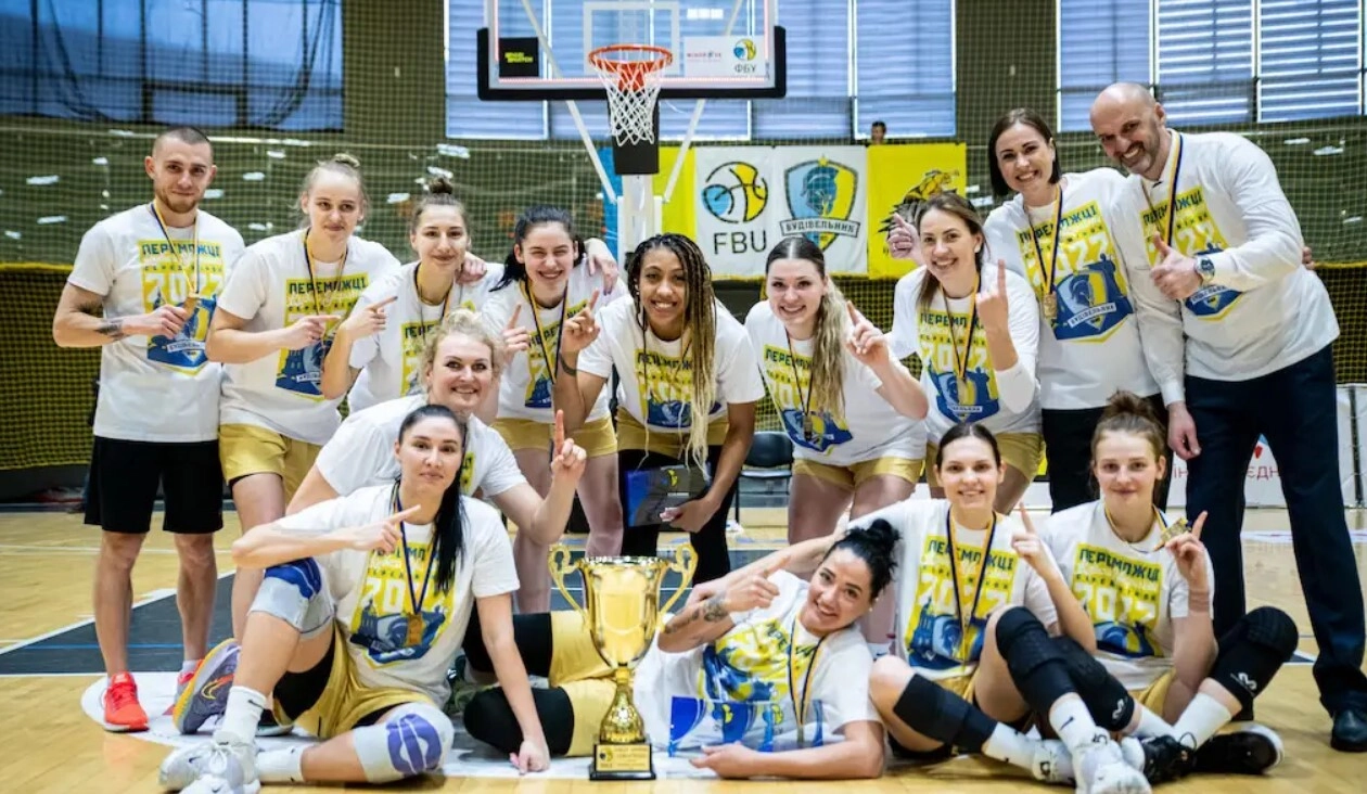 Жіноча баскетбольна команда святкує перемогу з кубком на спортивному майданчику