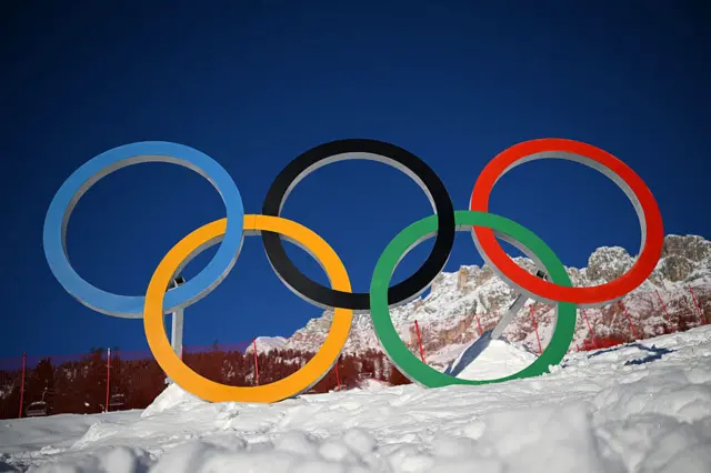 Олімпійські кільця на снігу під яскравим синім небом, символізуючи початок зимових Ігор 2026 року