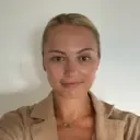 Жінка в бежевому піджаку на білому фоні, дивиться в камеру з легкою усмішкою