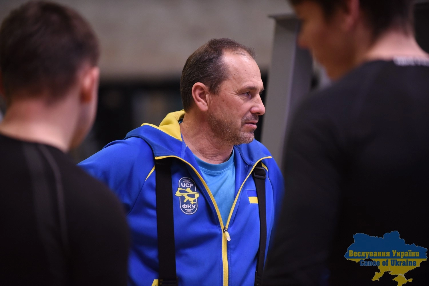 Тренер у синій спортивній формі з емблемою України спілкується з командою на тренуванні