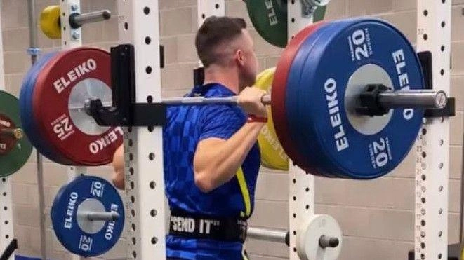 Спортсмен виконує присідання зі штангою в тренажерному залі, готуючись до змагань