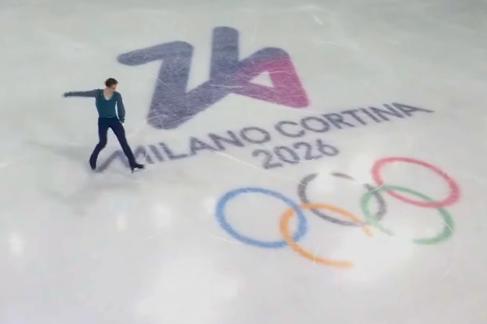 Фігурист виконує елемент на льоду з логотипом Мілано-Кортіна 2026 та олімпійськими кільцями