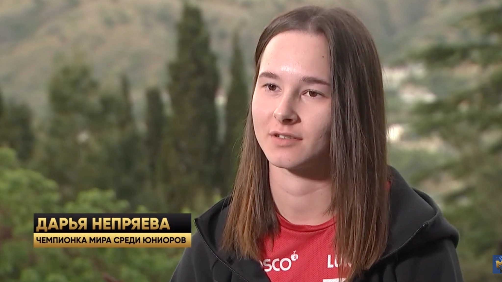 Жінка в червоній спортивній формі дає інтерв'ю на фоні природи, текст: Дар'я Непряєва, чемпіонка світу серед юніорів