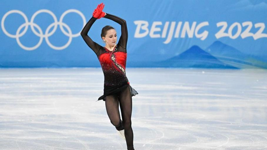 Фігуристка виконує елемент на льоду під час зимових Олімпійських ігор, на задньому плані олімпійські кільця