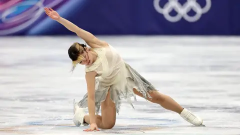 Фігуристка виконує елемент на льоду під час Зимових Олімпійських ігор, піднявши руку вгору