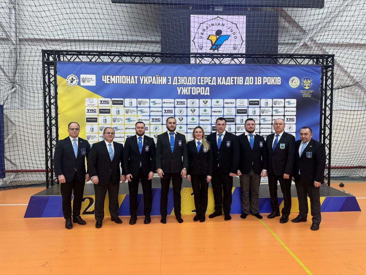 Судді чемпіонату України з дзюдо серед кадетів до 18 років на фоні банера з логотипами спонсорів