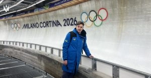 Чоловік у синій куртці стоїть біля треку з написом "Milano Cortina 2026" та олімпійськими кільцями
