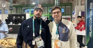 Двоє чоловіків у спортивному одязі стоять на фоні стенду "Milano Cortina 2026" на Зимовій Олімпіаді