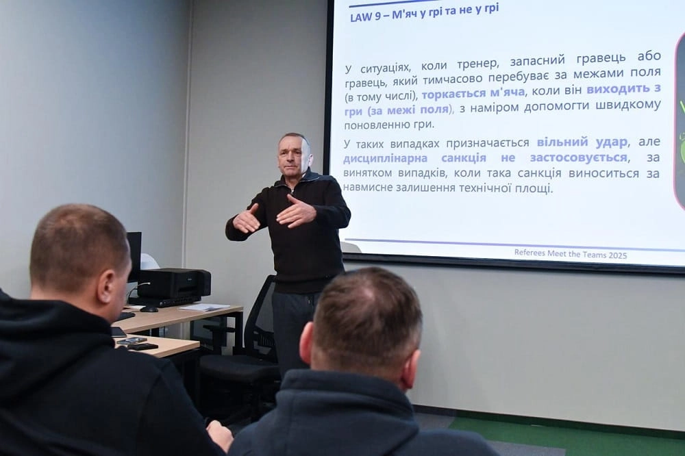 Тренер проводить семінар для тренерів у залі, обговорюючи зміни до Правил гри на екрані