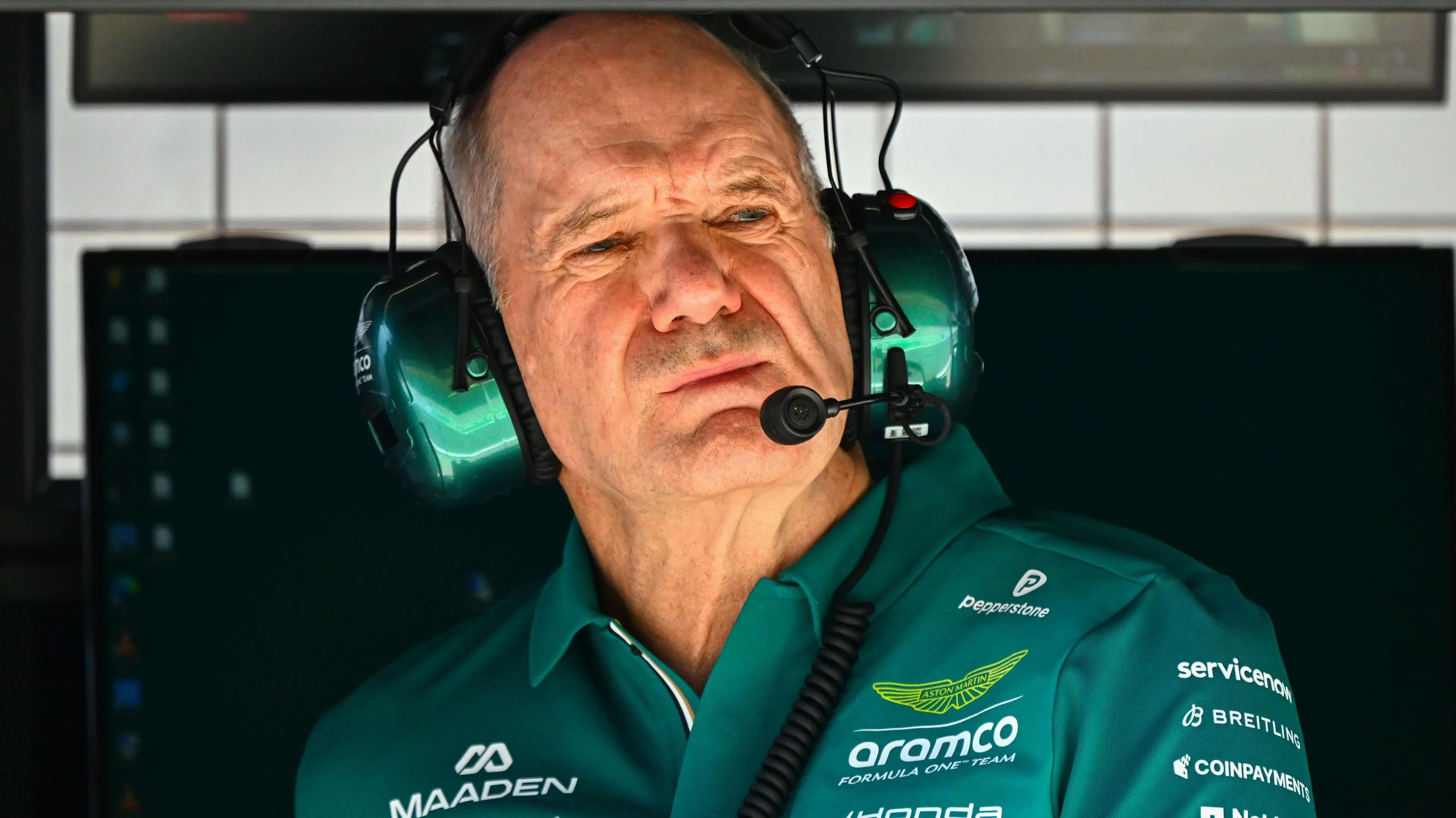 Чоловік у зеленій формі Aston Martin з навушниками спостерігає за тестуванням боліда Формули 1