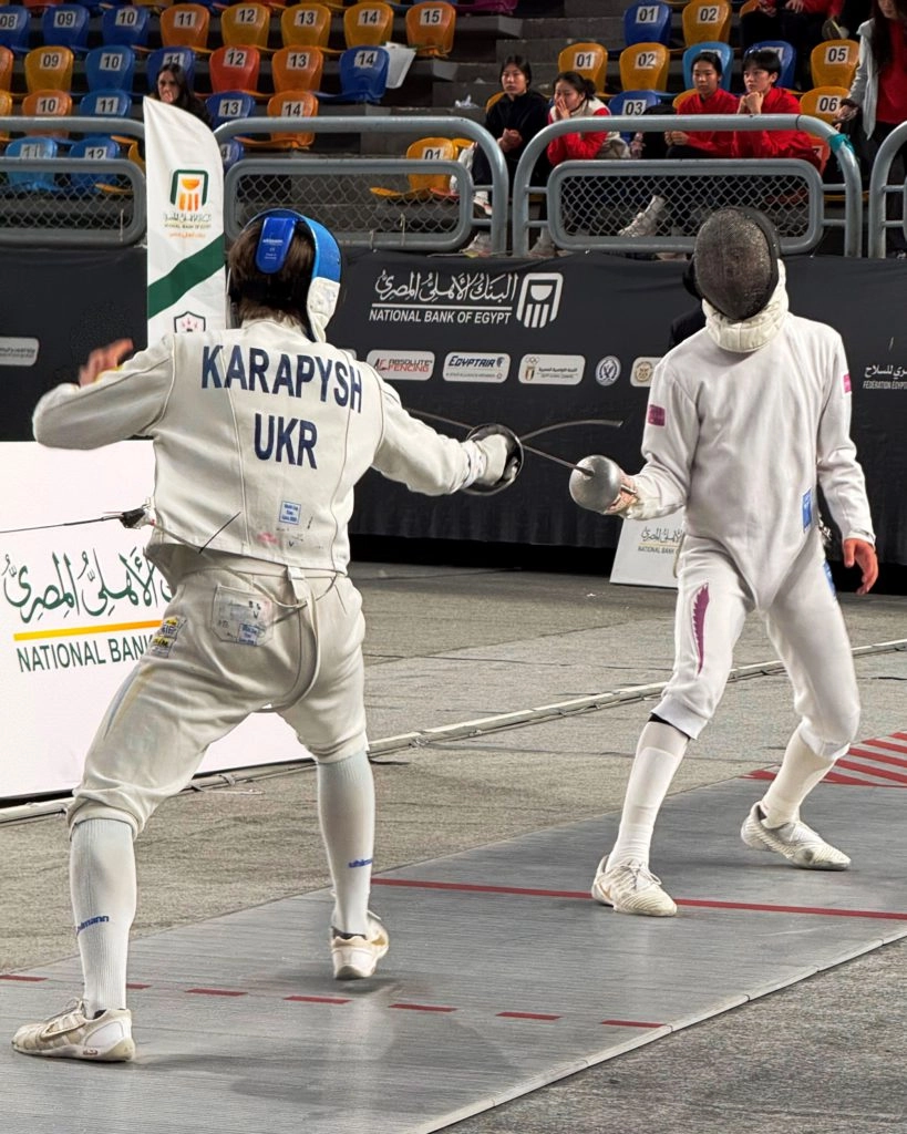 Український фехтувальник у білому костюмі змагається на юніорському Кубку світу в Каїрі