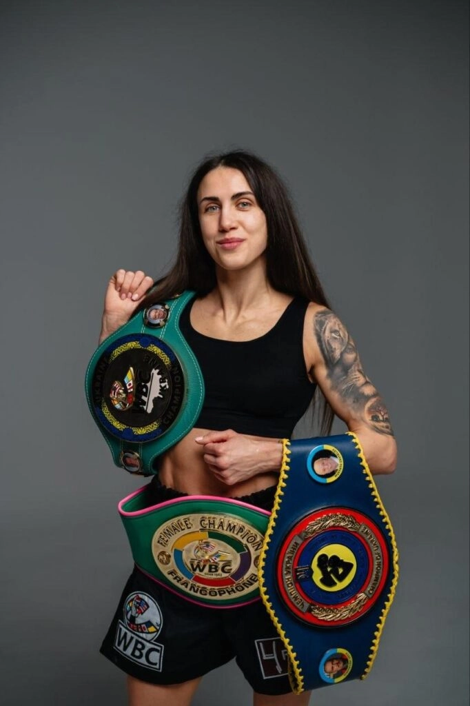Українська боксерка Анастасія Петренко з чемпіонськими поясами WBC та IBO на сірому фоні