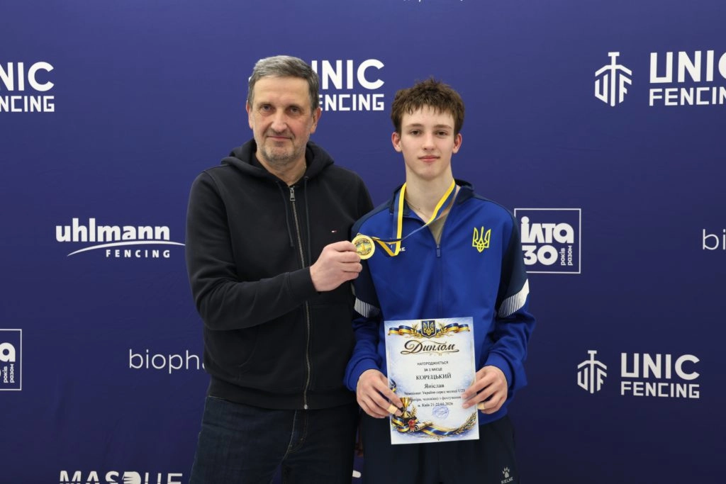 Чоловік та юнак з медаллю та дипломом на фоні банера чемпіонату України з фехтування U-23