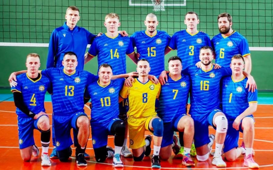 Волейбольна команда у синьо-жовтій формі позує перед сіткою на спортивному майданчику