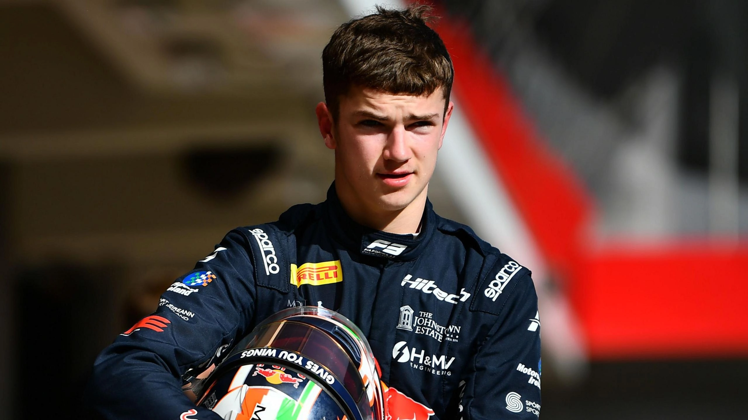 Молодий гонщик у формі Red Bull тримає шолом, готуючись до сезону Формули 3 на гоночній трасі