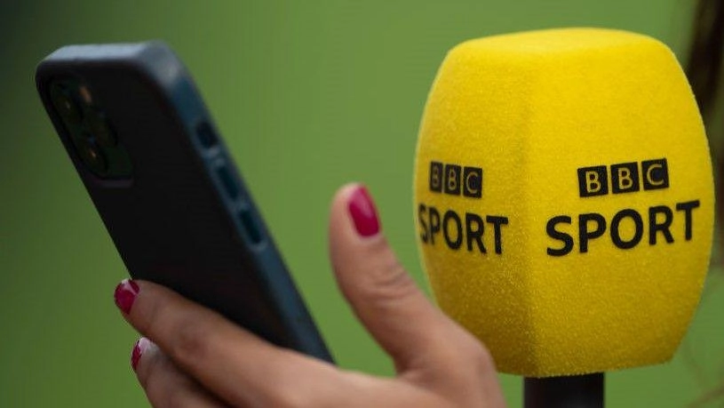Мікрофон BBC Sport та рука з телефоном на зеленому фоні під час інтерв'ю або репортажу