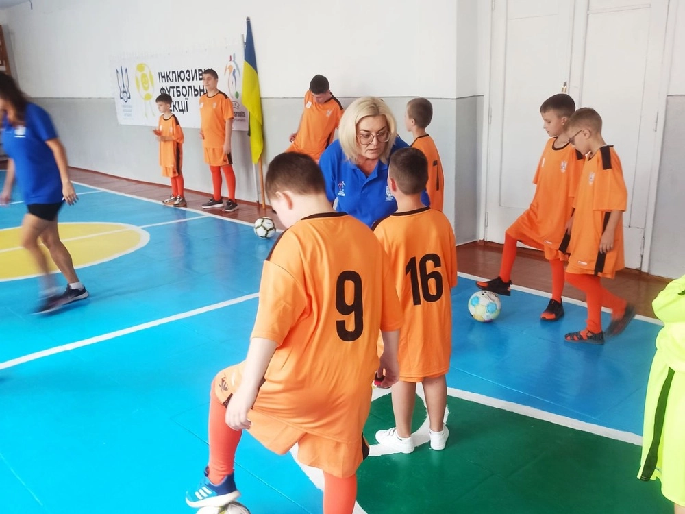 Діти в оранжевій формі тренуються з м'ячами в спортивному залі під керівництвом тренера