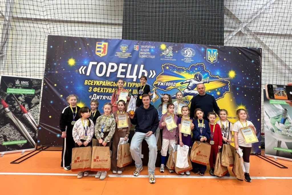 Юні фехтувальники з нагородами на турнірі "Горець" в Ужгороді, радісно позують на фоні банера