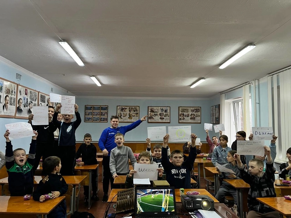 Діти в класі тримають плакати, усміхаються, на столі ноутбук із зображенням футбольного поля