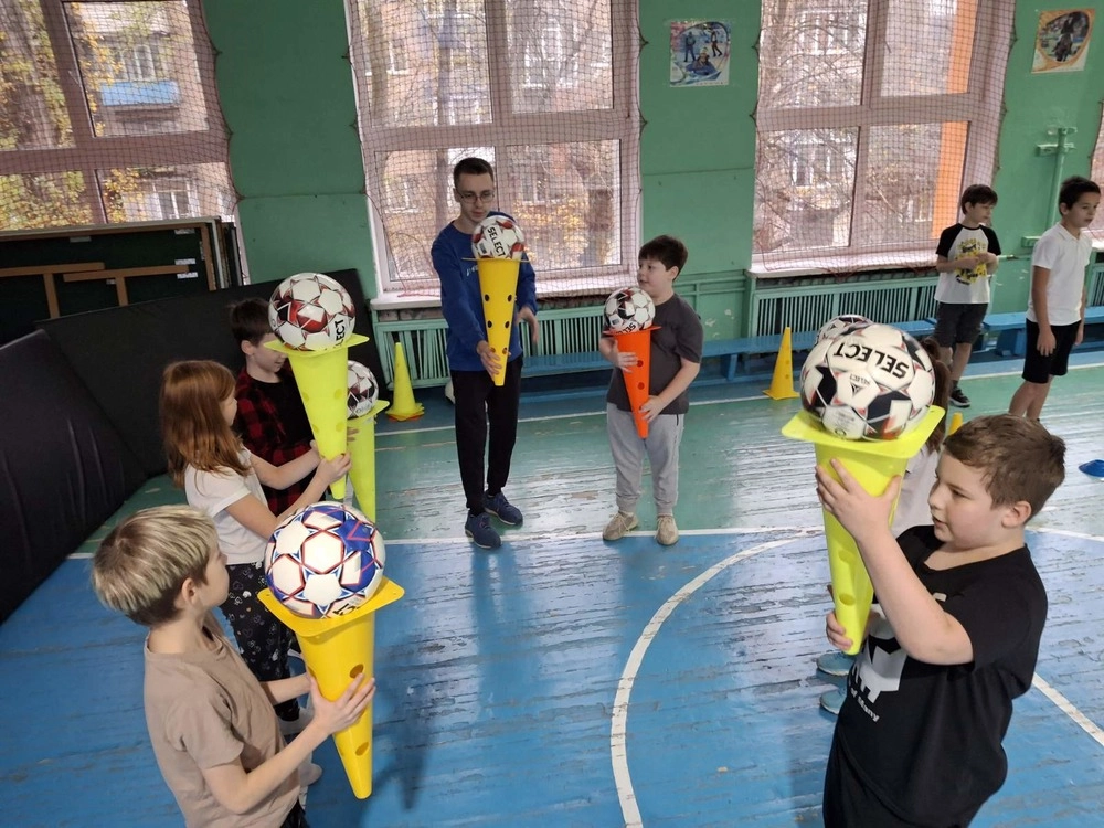 Діти у спортивній залі тримають футбольні м'ячі на конусах, навчаючись у молодіжному футбольному хабі