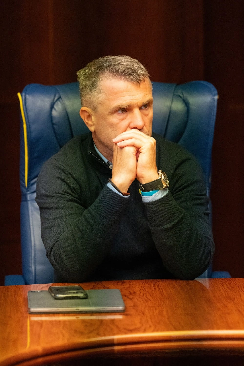 Тренер сидить за столом у кріслі, задумливо дивлячись перед собою, на нараді в Будинку футболу