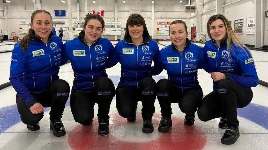 Британська команда з керлінгу в синій формі позує на льодовій арені перед грою