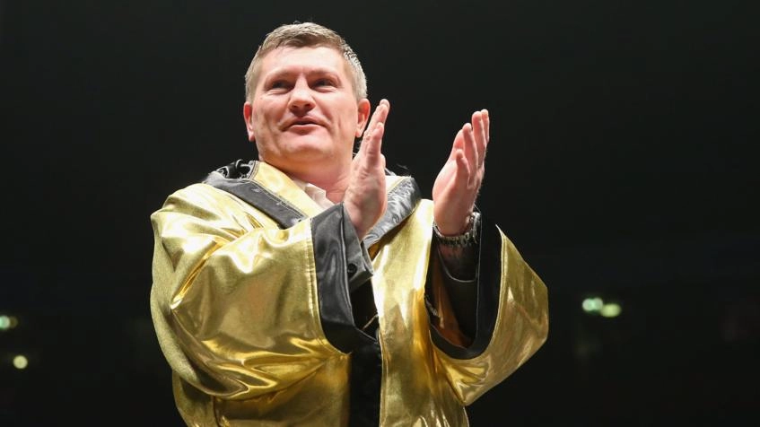Колишній боксер у золотому халаті аплодує на рингу, усміхаючись під час заходу