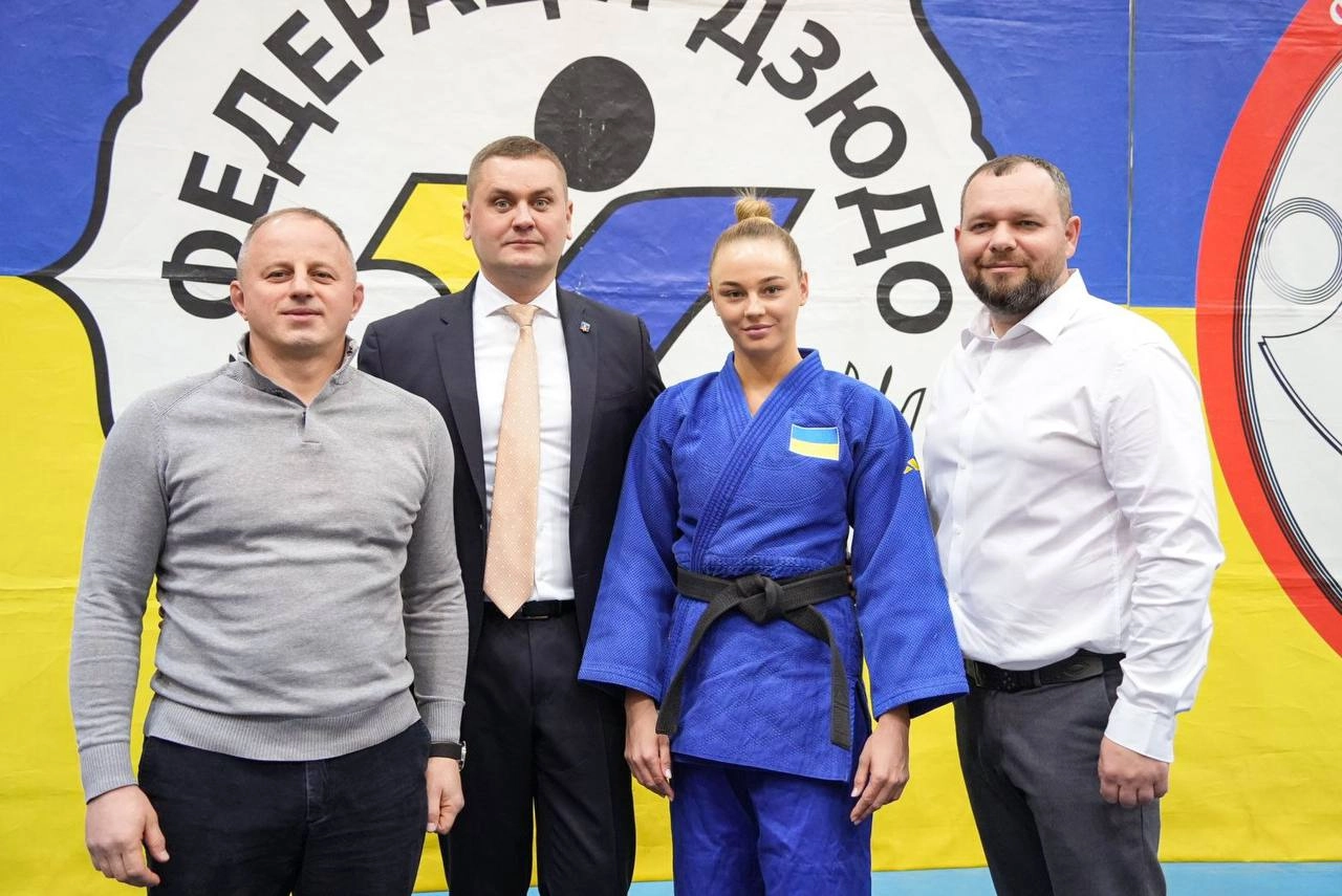 Чотири людини на фоні банера Федерації дзюдо України, спортсменка у синьому кімоно з нагородою