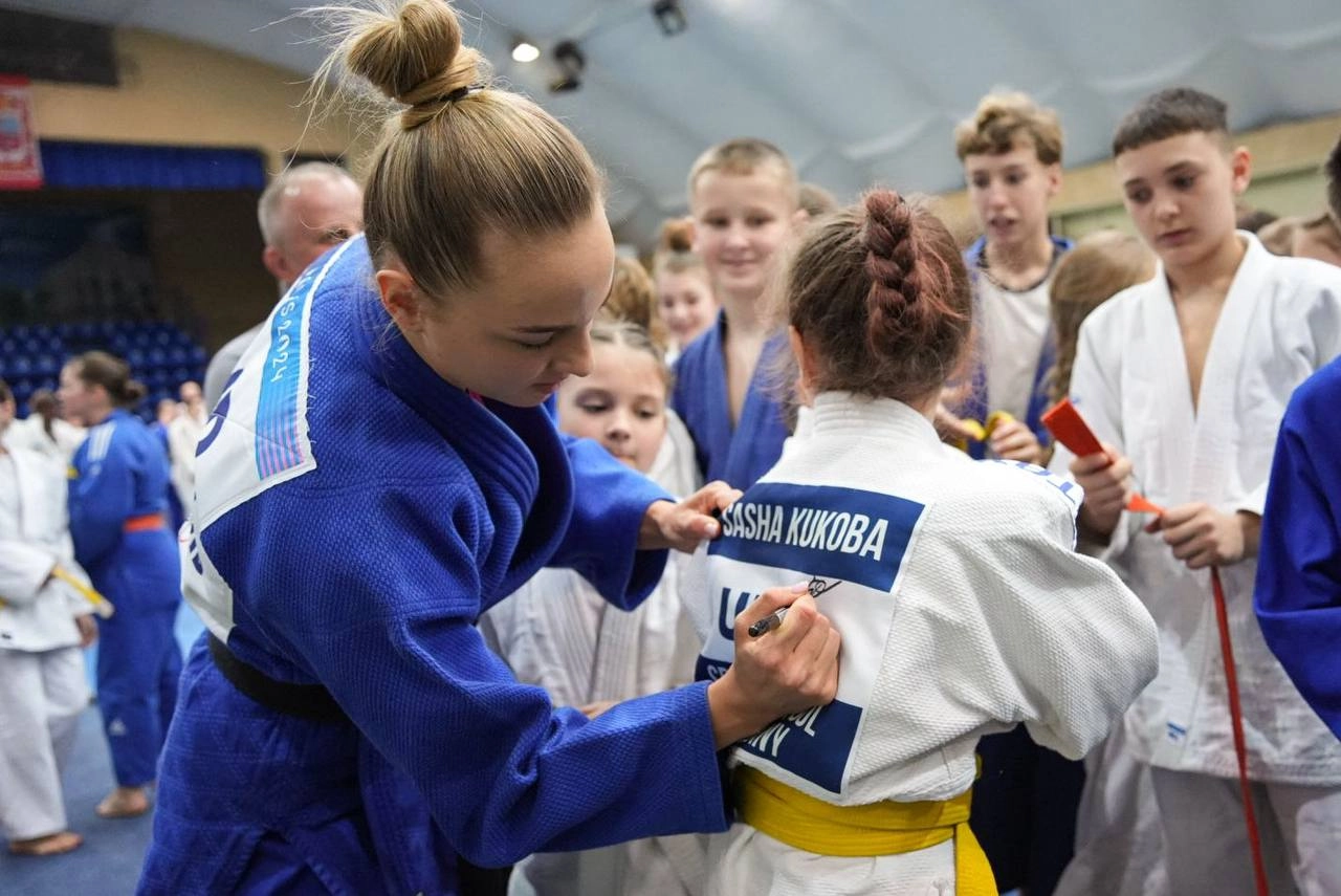 Чемпіонка дзюдо підписує кімоно юної учасниці майстер-класу в Черкасах, оточена іншими дітьми