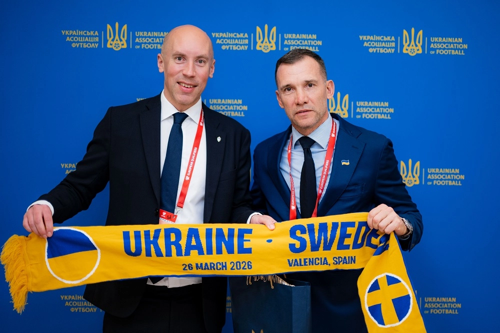 Двоє чоловіків тримають шарф з написом "Ukraine - Sweden" на фоні логотипів футбольних асоціацій