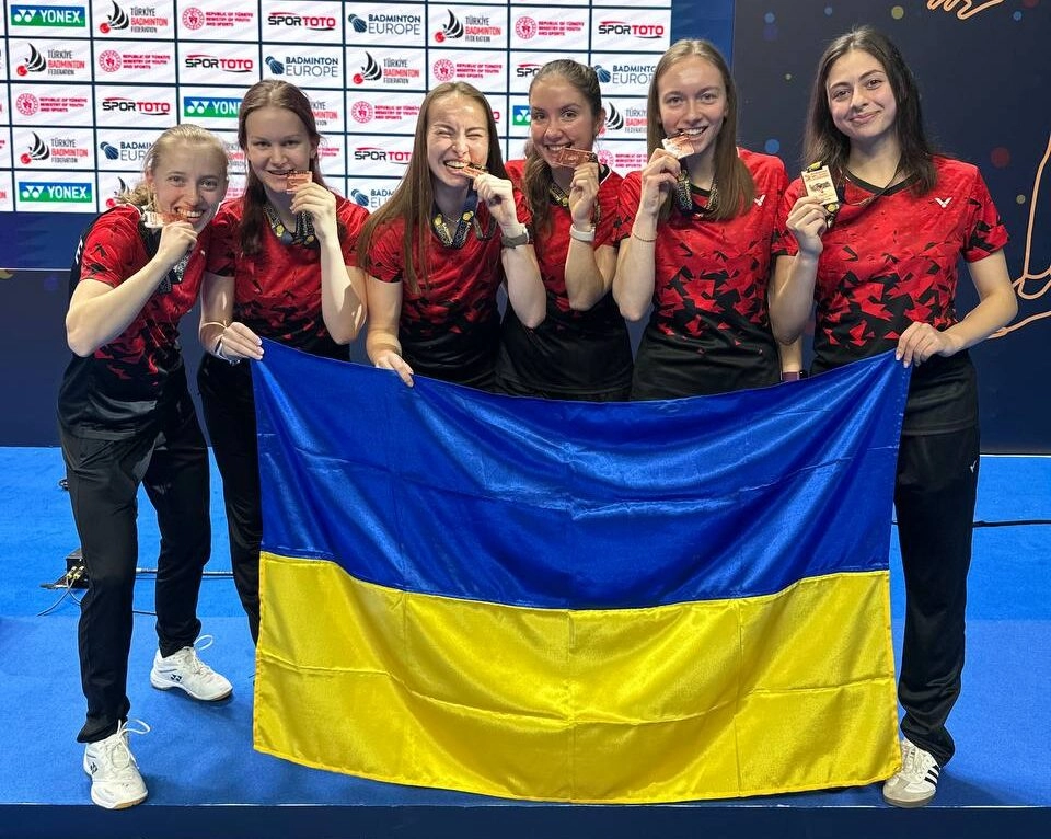 Українська жіноча збірна з бадмінтону святкує бронзову медаль на Чемпіонаті Європи, тримаючи прапор України