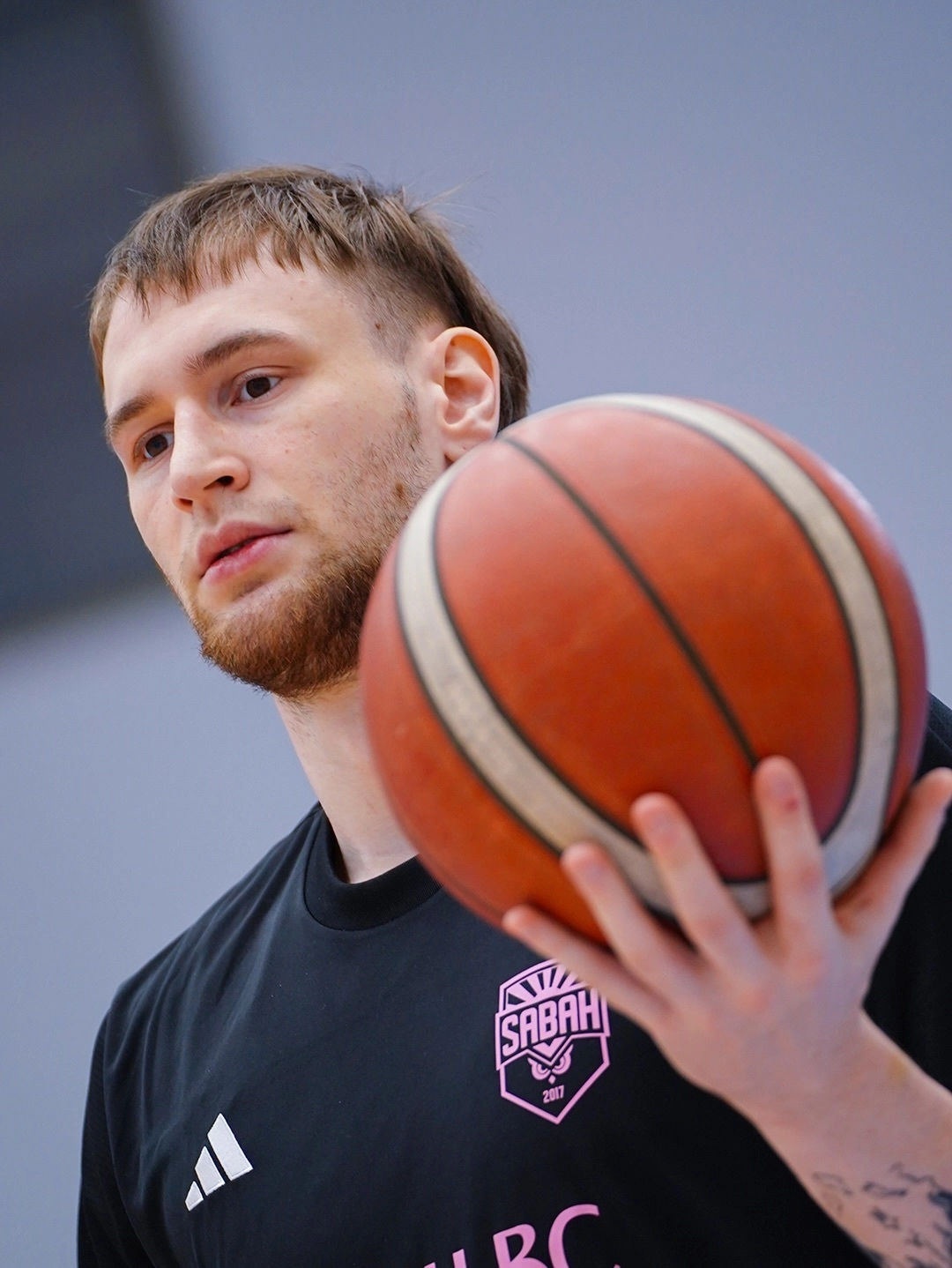 Баскетболіст у чорній формі з м'ячем у руках готується до гри, зосереджено дивлячись вперед